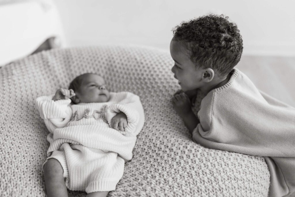 Big brother looking at his newborn brother on the newborn bean bag in the white room studio