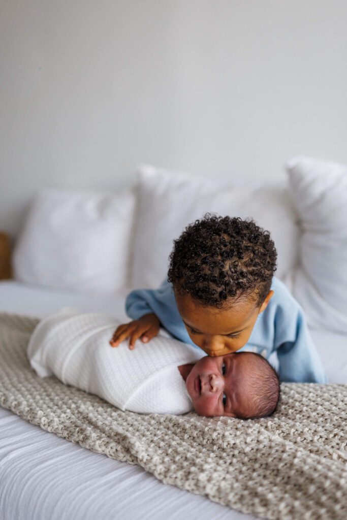 big brother kissing newborn baby brother on the cheek.