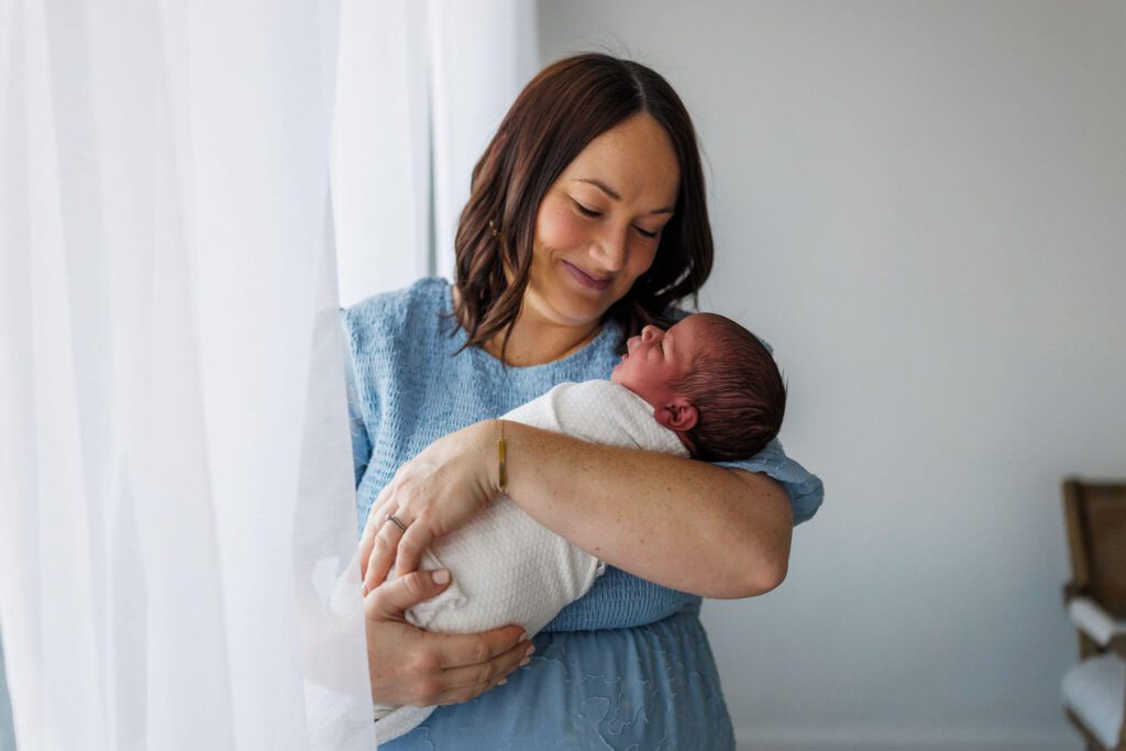 mom holding newborn against the curtains
