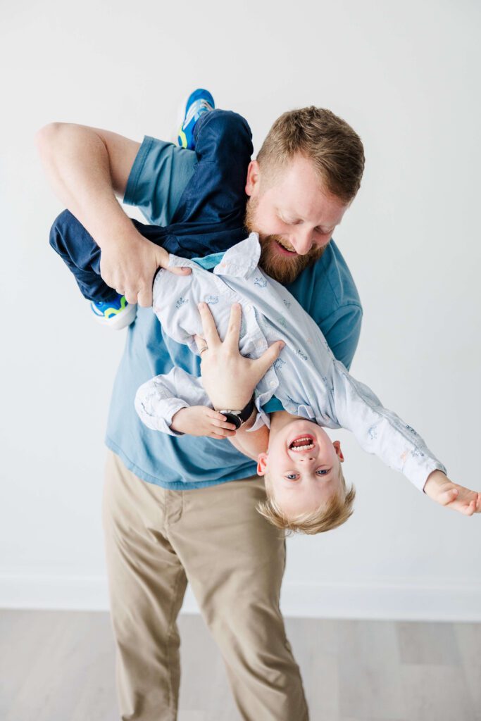 dad flipping son upside down against the white room wall