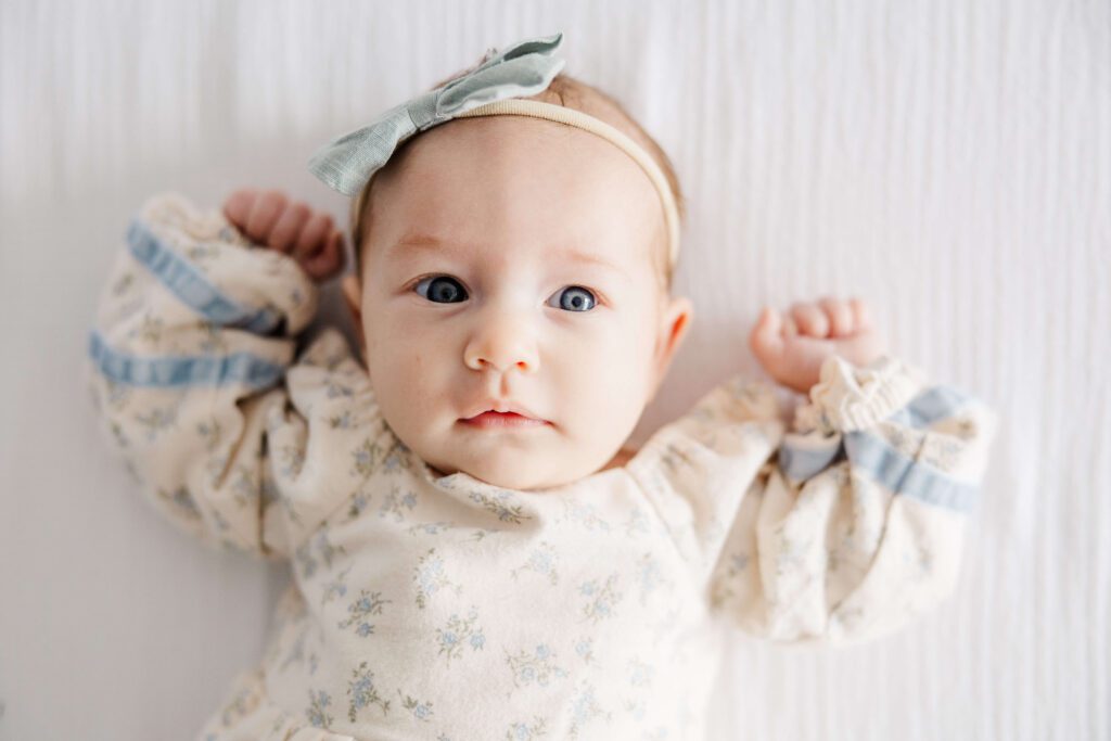 baby laying on bed staring up at the camera. 